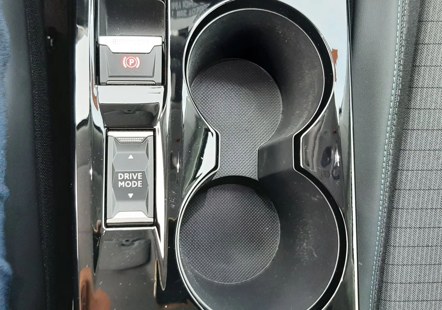 Gros plan sur la console centrale noire brillante de la Peugeot 2008 gris, avec porte-gobelets et boutons Drive Mode et frein à main électrique.