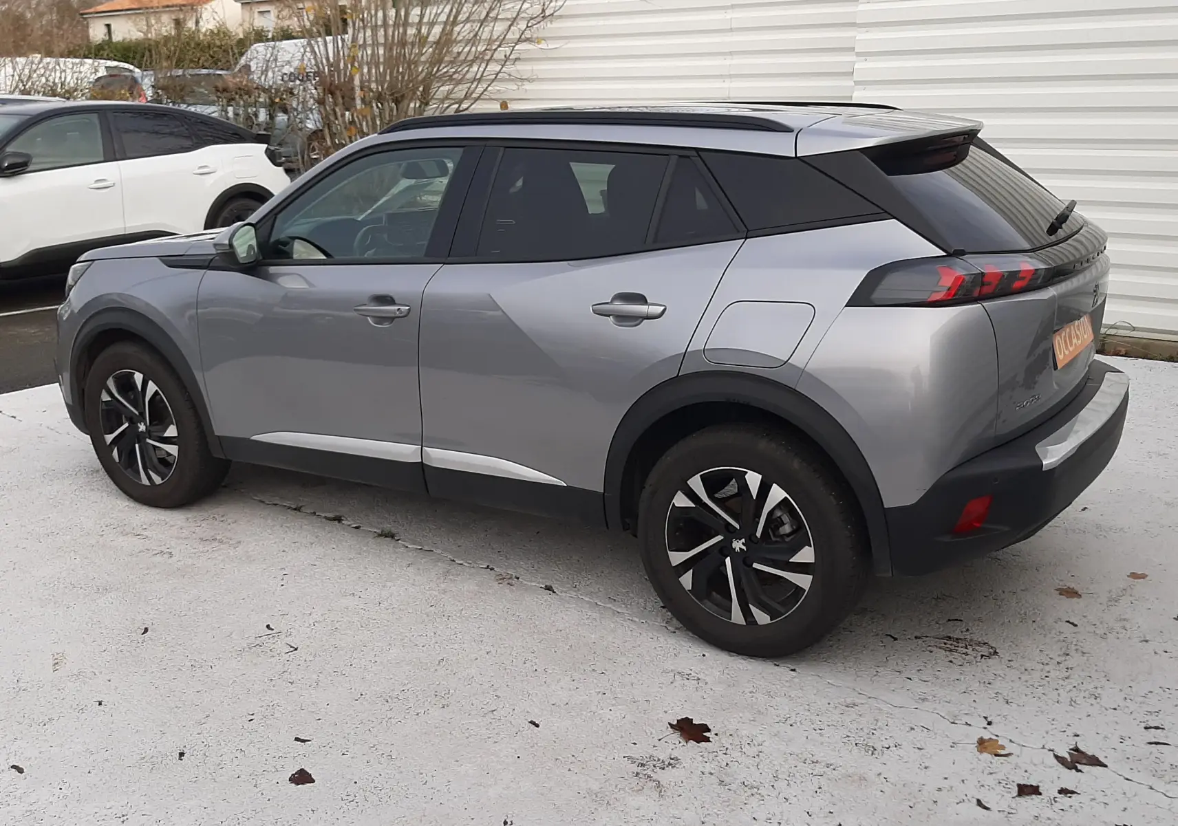 Peugeot 2008 gris vue 3/4 arrière droit, toit noir contrasté et jantes alliage bicolores sur parking.
