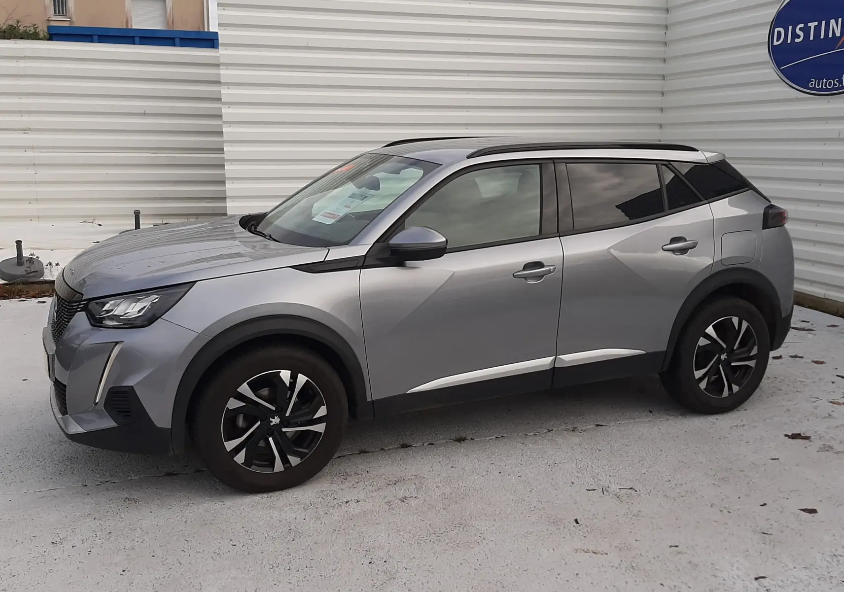 Peugeot 2008 gris en vue de profil côté gauche, soulignant ses jantes noires et toit panoramique foncé.