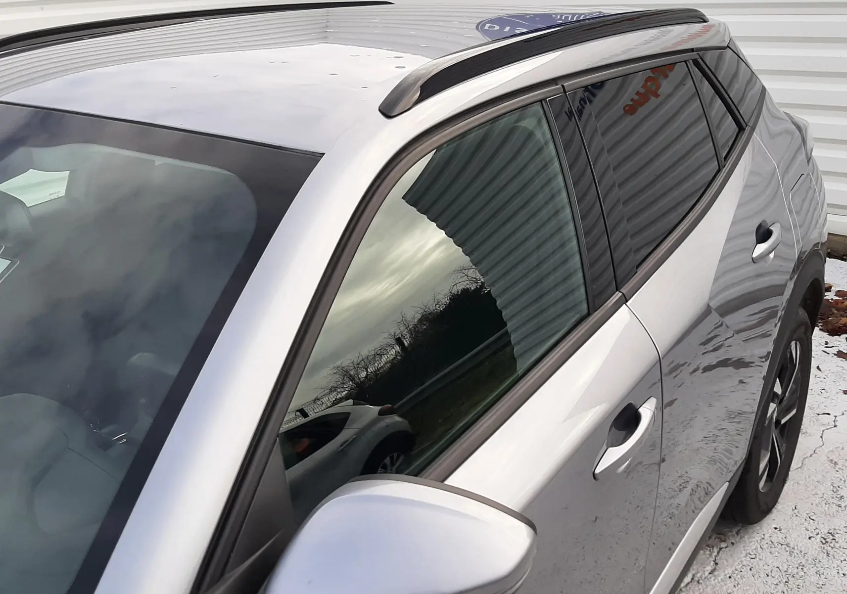 Vue rapprochée côté gauche arrière du Peugeot 2008 gris 2021 avec toit noir et barres de toit noires.