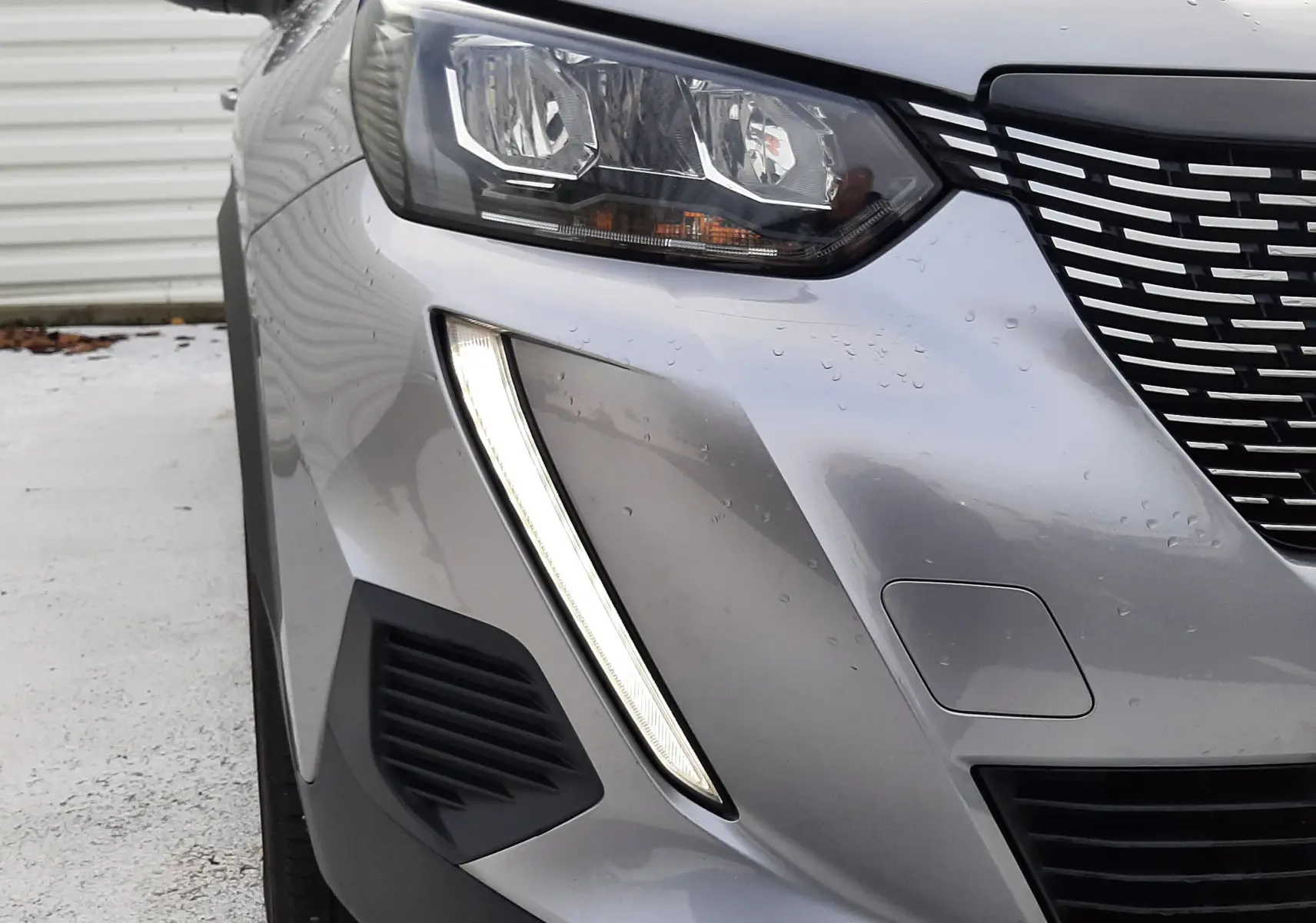 Gros plan sur l'avant gauche gris du Peugeot 2008 2021, mettant en valeur son phare et sa signature lumineuse verticale LED.