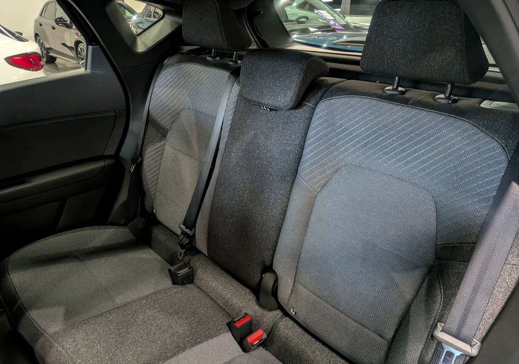 Vue intérieure sur les sièges arrière en tissu gris du Renault Captur Mild Hybrid 2025, avec ceintures et appuie-têtes visibles.