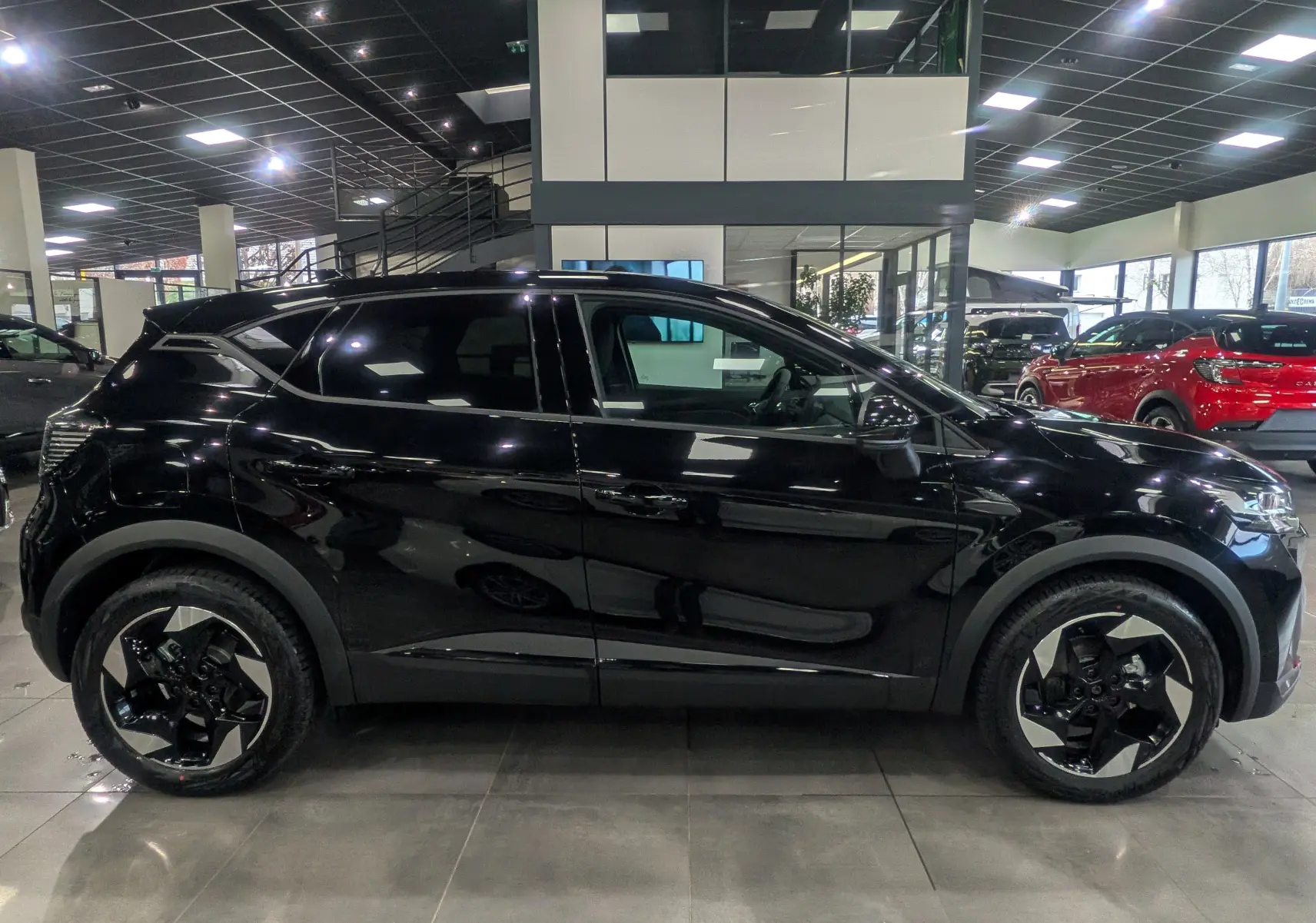 Profil côté gauche du Renault Captur noir 2025 Mild Hybrid avec jantes bi-ton et toit noir en showroom.