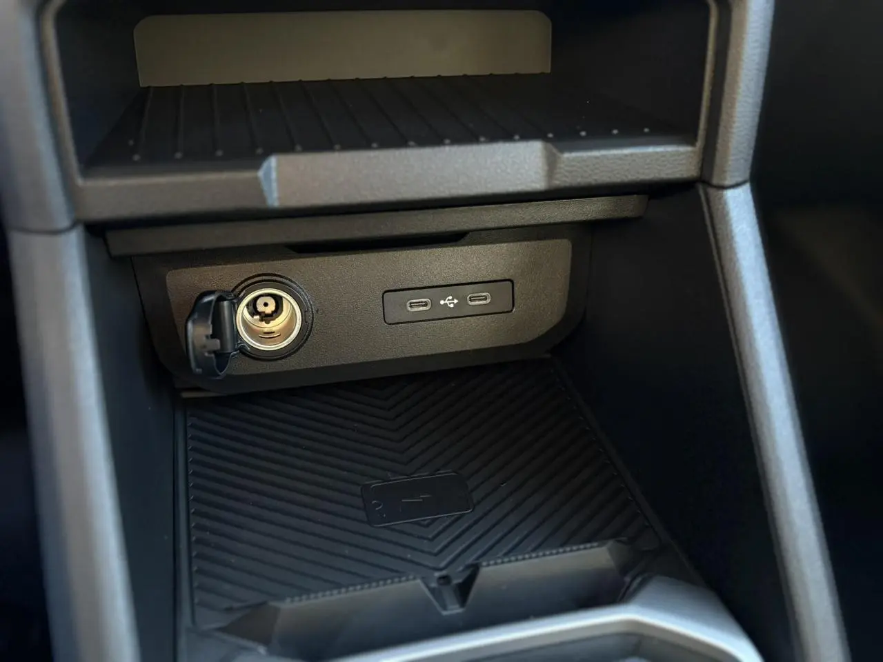 Gros plan sur la console centrale du Dacia Duster 2026, montrant prise allume-cigare, ports USB et zone de charge sans fil.