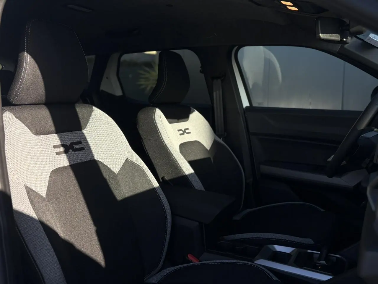 Vue intérieure côté gauche montrant les sièges avant noirs et gris avec logo Dacia sur appuie-tête.