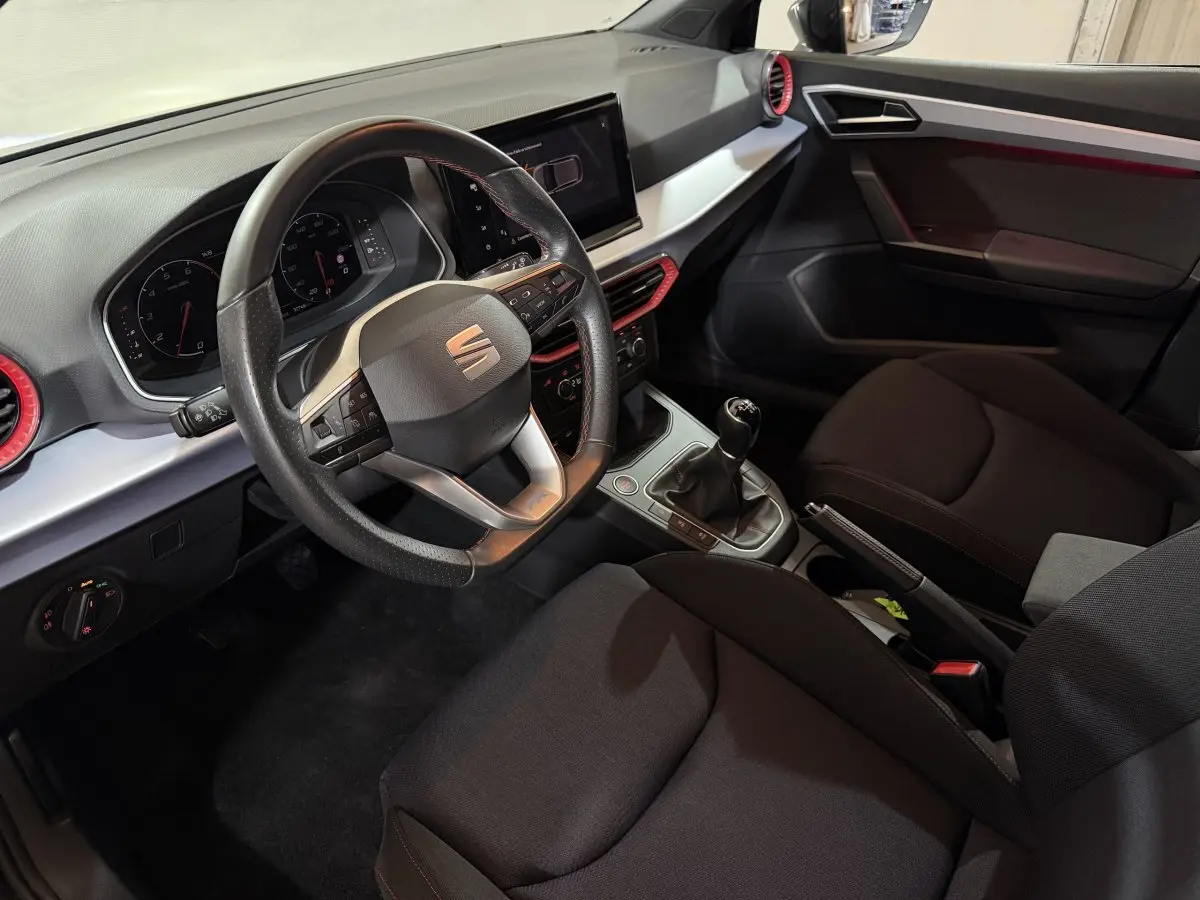 Vue intérieure côté conducteur de la SEAT Ibiza 1.0 TSI 110 FR 2024, volant cuir alu multifonctions et tableau de bord noir avec touches rouges.