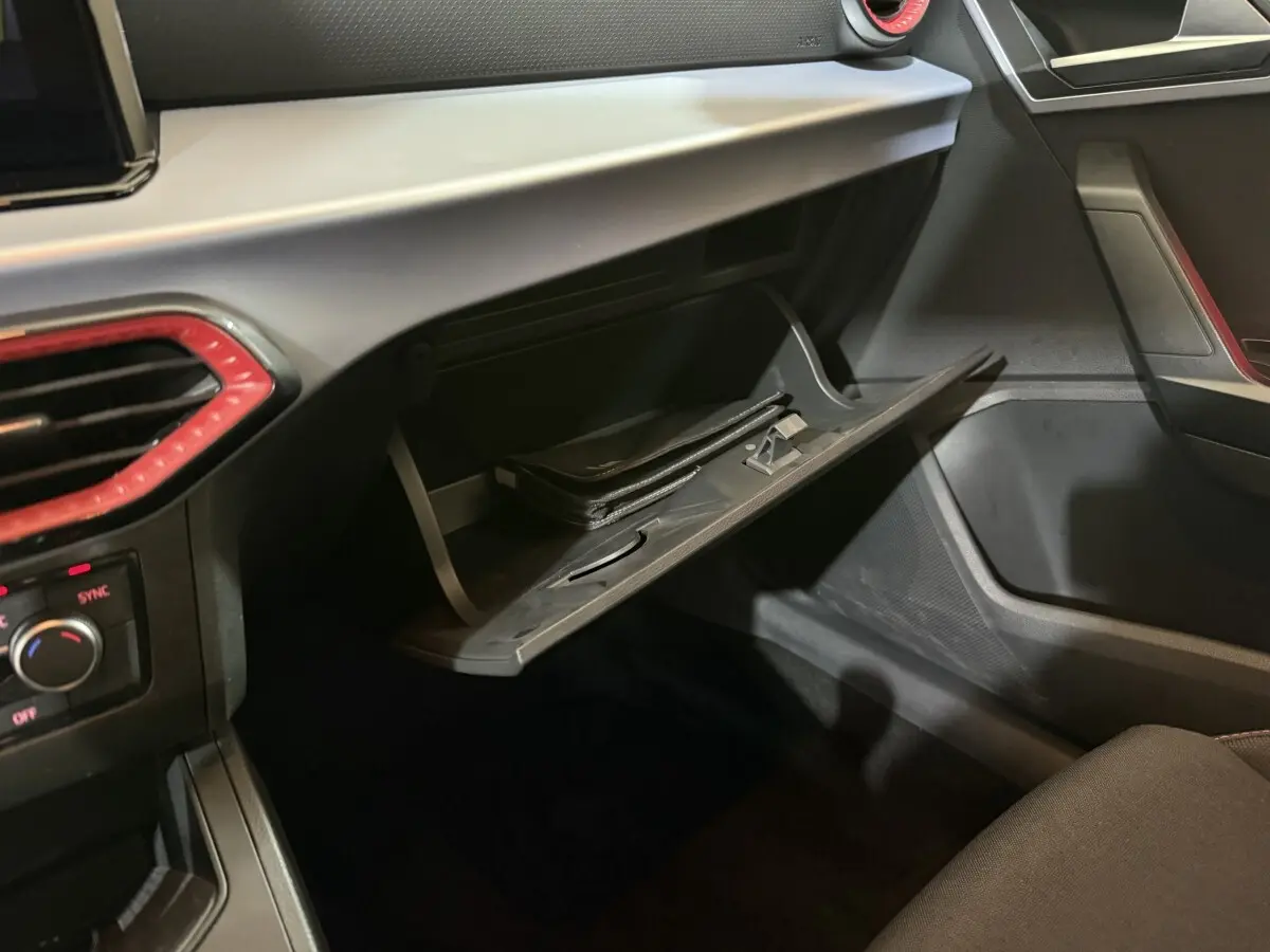 Intérieur SEAT Ibiza 2024 noir, vue côté passager sur la boîte à gants ouverte avec pochette noire visible.