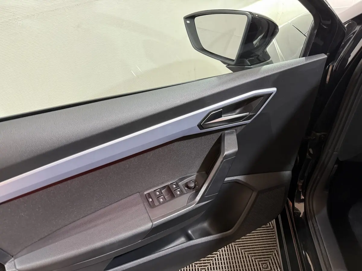 Vue intérieure côté gauche de la porte noire d'une SEAT IBIZA 1.0 TSI 110 FR avec commandes électriques et rétroviseur intégré.