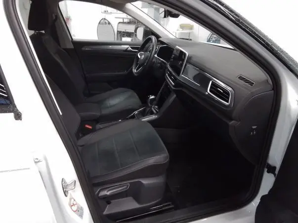 Vue intérieure côté conducteur du Volkswagen T-Roc blanc toit noir 2025, montrant sièges et tableau de bord modernes.