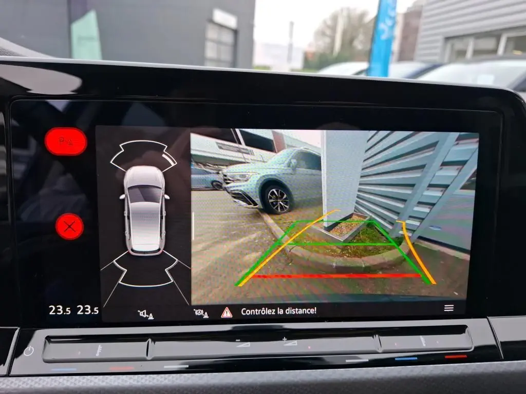 Vue écran caméra de recul d'une Volkswagen Golf gris 2022, affichant les lignes de guidage et un obstacle côté droit.