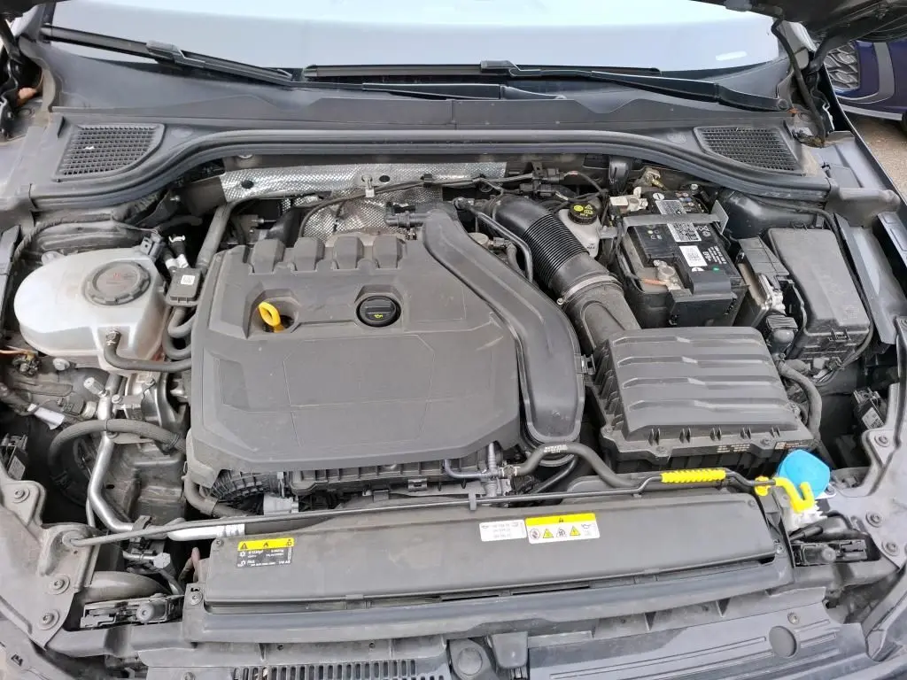 Vue plongeante sur le moteur essence gris d'une Volkswagen Golf 1.5 eTSI 130 DSG7 Active, avec batterie et réservoir visibles.