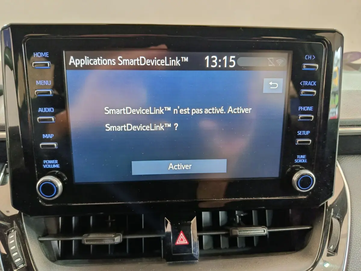 Gros plan sur l'écran tactile central noir de la Toyota Corolla Hybride 122h Active affichant le menu SmartDeviceLink à activer.