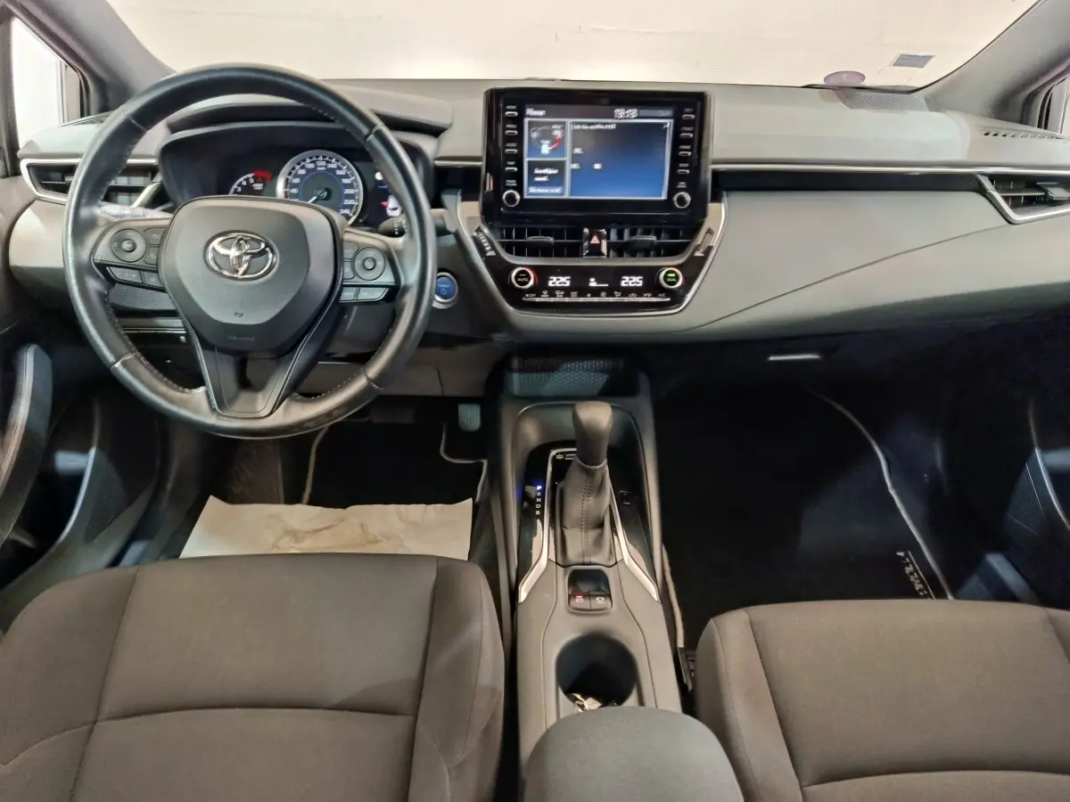 Vue intérieure avant de la Toyota Corolla Hybride 122h, tableau de bord avec écran tactile et volant multifonctions cuir noir.