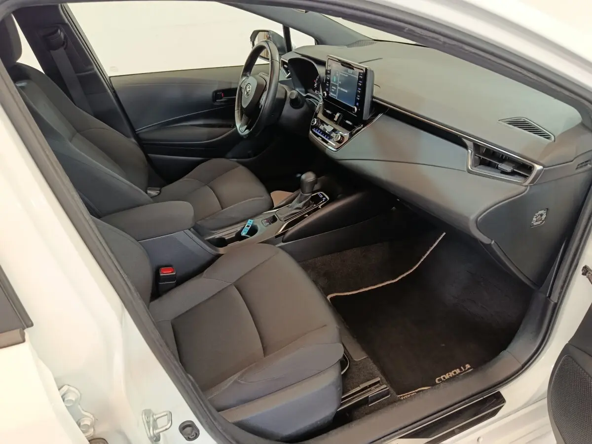 Intérieur avant droit de la Toyota Corolla Hybride blanche, montrant sièges noirs et tableau de bord avec écran tactile central.