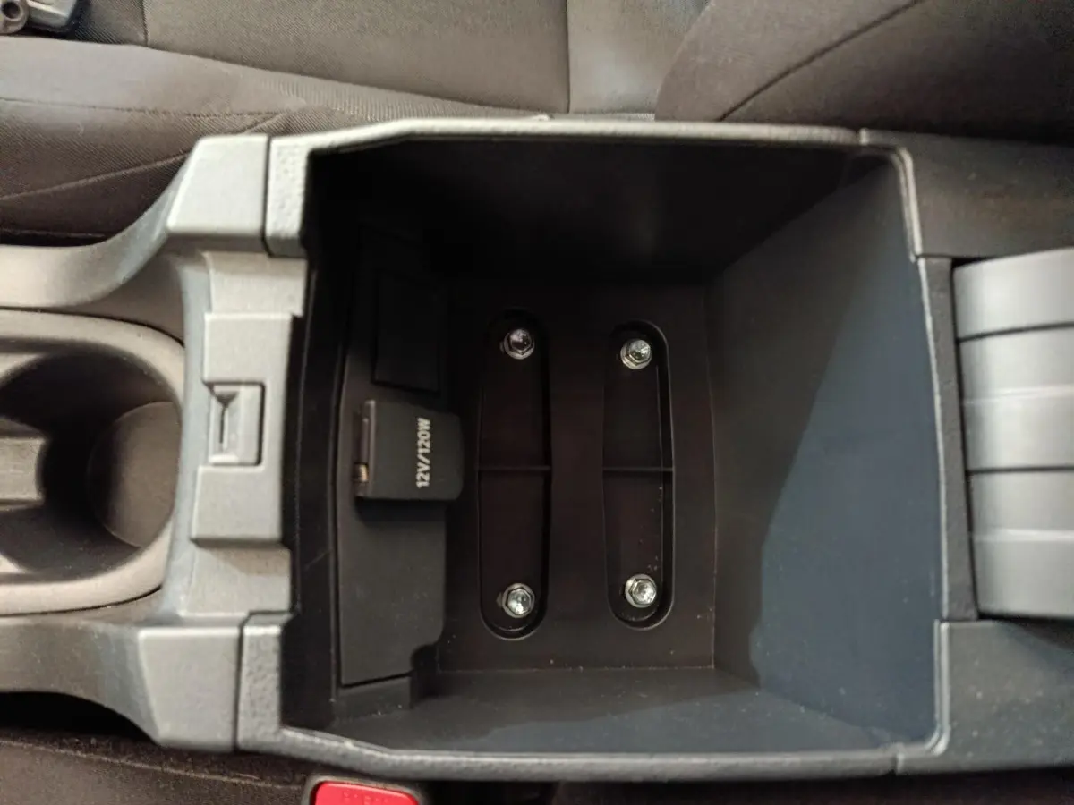 Vue plongeante sur le rangement central noir de la Toyota Corolla Hybride 122h Active, avec prise 12V visible.