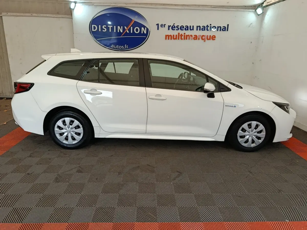 Vue latérale droite d'une Toyota Corolla Hybride 122h Active blanche en version break, avec jantes acier et badges hybrides visibles.