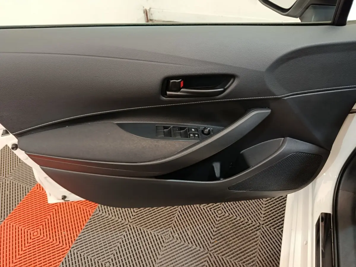 Vue intérieure côté gauche de la porte avant d’une Toyota Corolla Hybride blanche, avec commandes de vitres et poignée noire.
