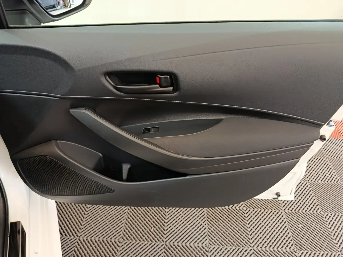 Gros plan sur la porte intérieure côté gauche noire de la Toyota Corolla Hybride 122h Active blanche, avec poignée et haut-parleur intégrés.