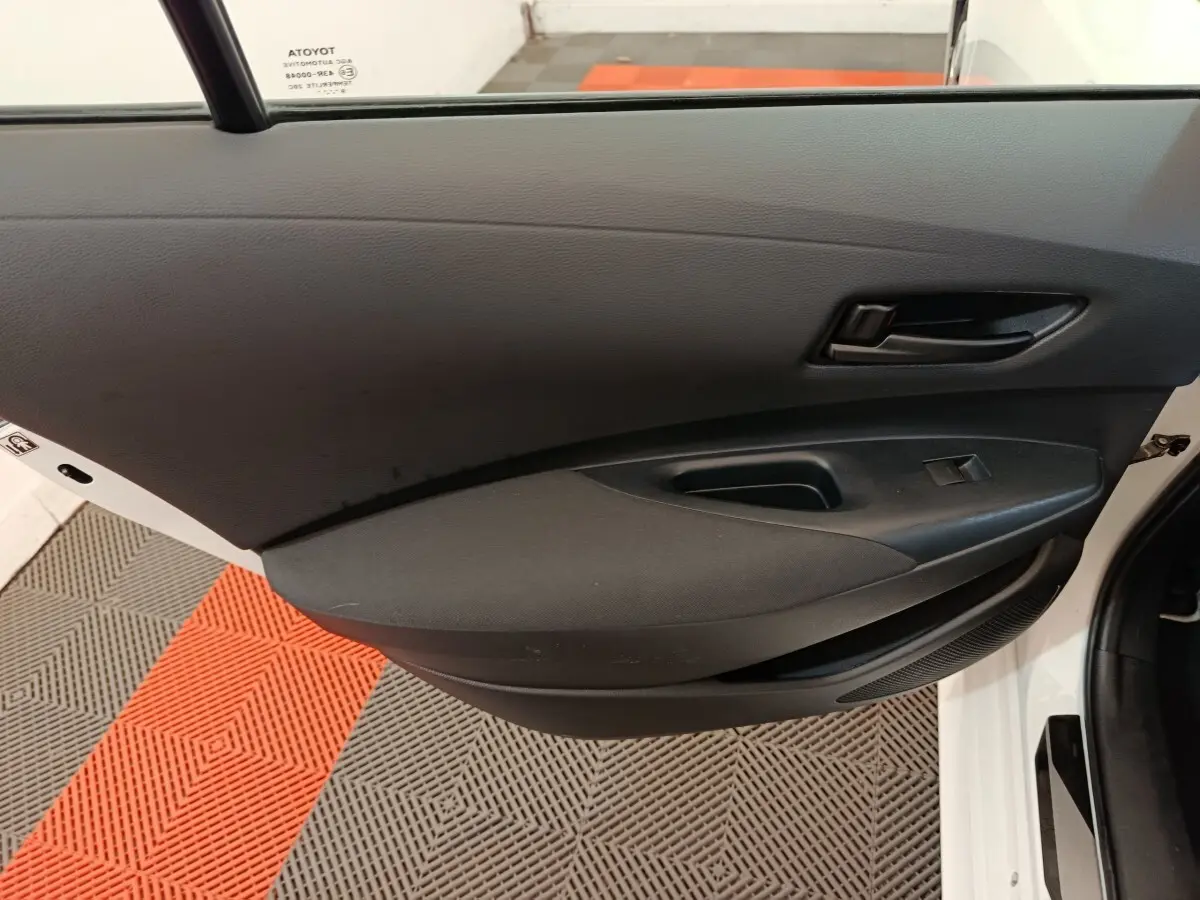 Vue rapprochée de la porte avant gauche noire intérieure d’une Toyota Corolla Hybride blanche, avec poignée et commande de vitre.