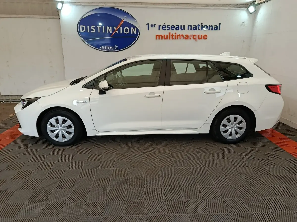 Profil côté gauche d'une Toyota Corolla Hybride 122h Active blanche, break avec jantes acier et rétroviseurs blancs.
