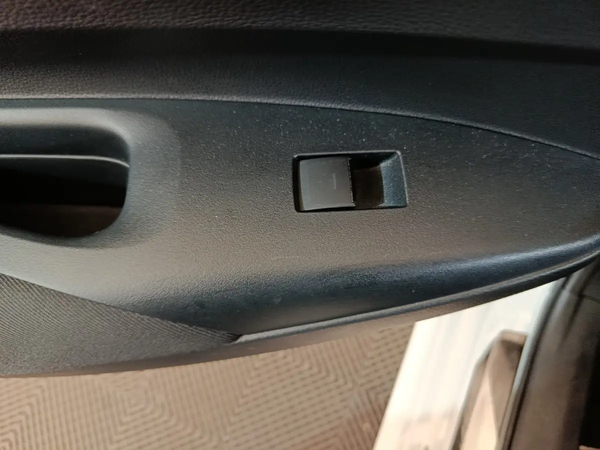 Gros plan sur la commande de lève-vitre côté droit d’une Toyota Corolla hybride blanche, intérieur noir.