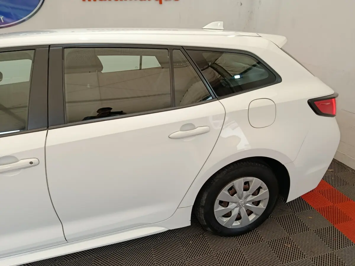 Vue latérale côté gauche sur l'arrière d'une Toyota Corolla hybride blanche avec feux arrière LED et jante acier.