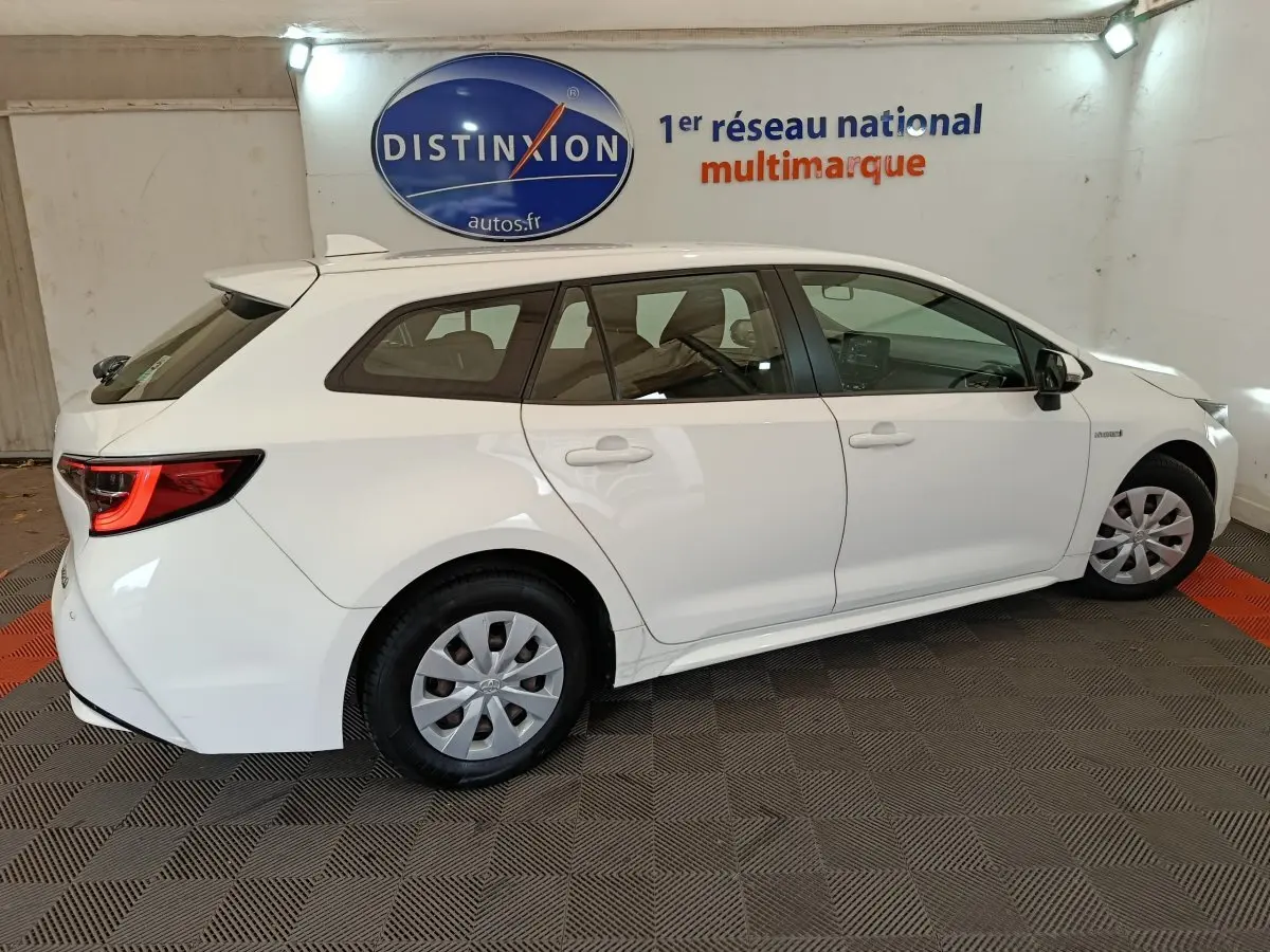 Vue de profil côté droit d'une Toyota Corolla Hybride 122h Active blanche en version break, avec jantes acier et feux arrière LED.