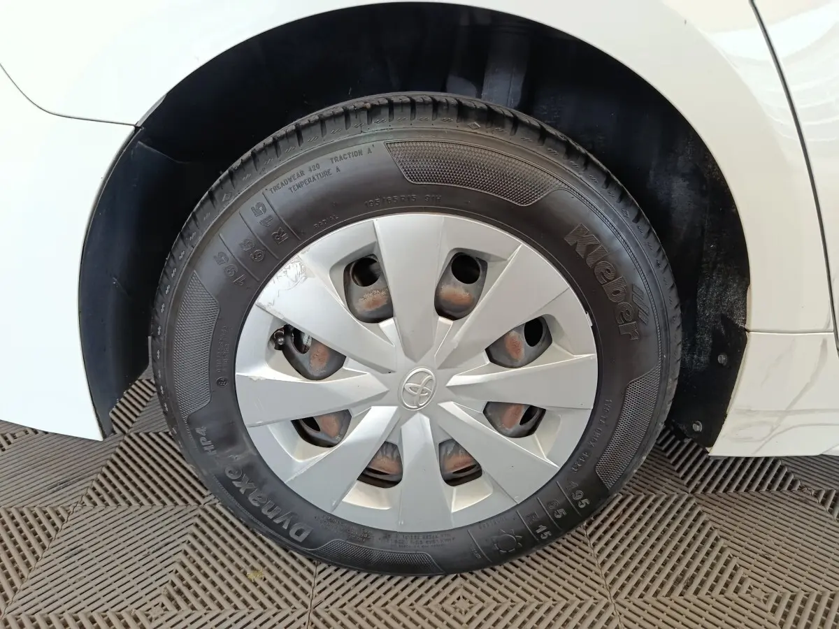 Gros plan sur la roue avant gauche blanche d'une Toyota Corolla Hybride 122h Active, avec enjoliveur argenté et logo Toyota.