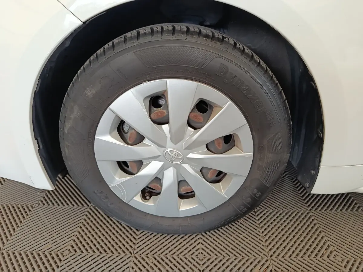 Gros plan sur la roue avant droite d'une Toyota Corolla Hybride blanche, avec enjoliveur gris et logo Toyota central.