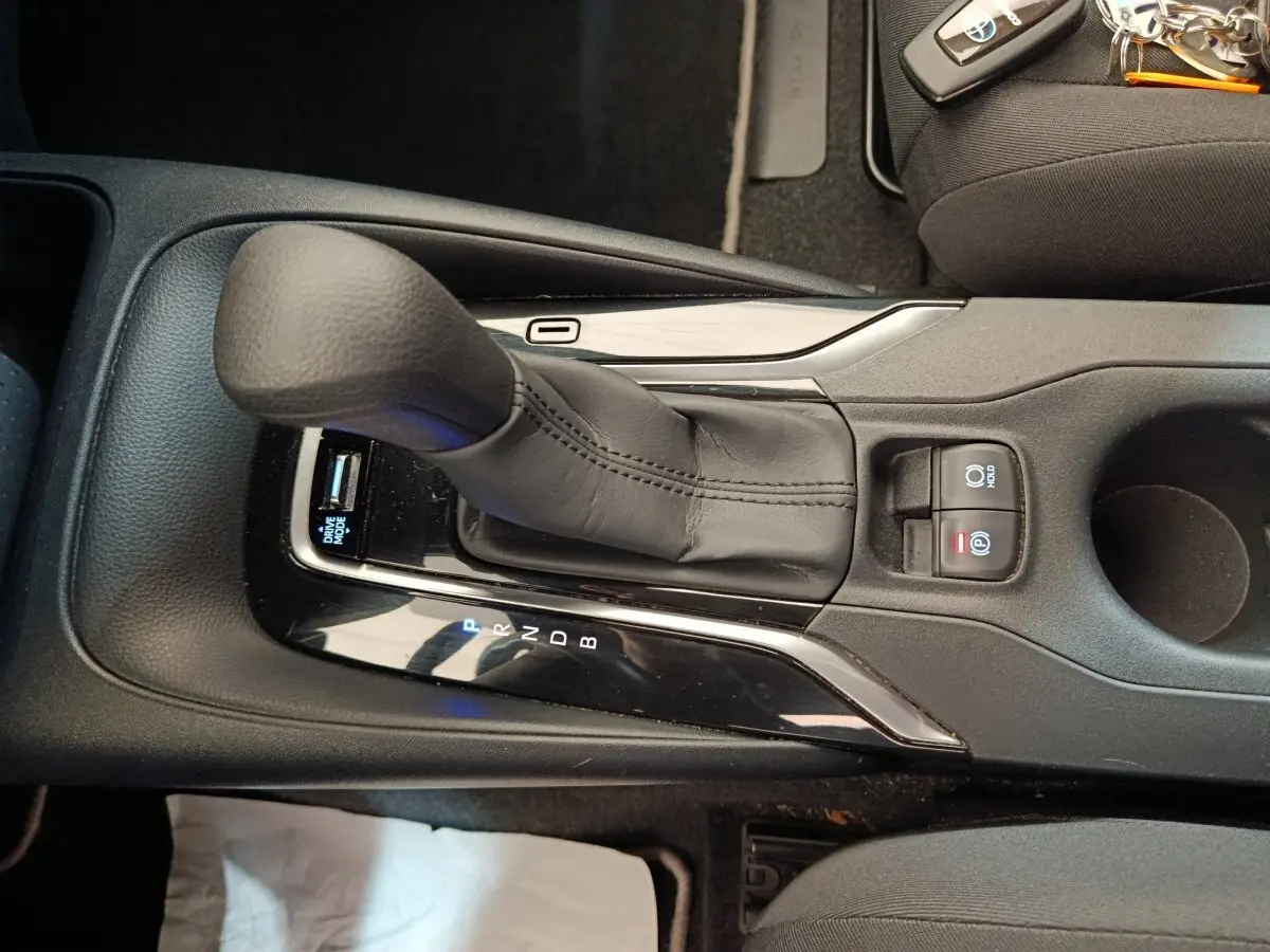 Vue rapprochée de la console centrale noire de la Toyota Corolla Hybride 2020 avec levier de vitesse automatique et boutons de frein à main électrique.