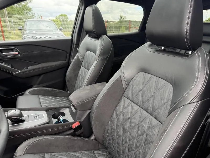 Vue intérieure côté avant droit du Nissan Qashqai 2024 avec sièges cuir noir matelassé et accoudoir central.