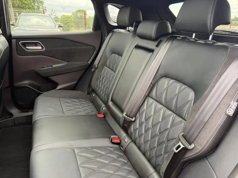 Vue intérieure du siège arrière en cuir noir matelassé du Nissan Qashqai 2024, avec ceintures de sécurité et porte arrière visible.