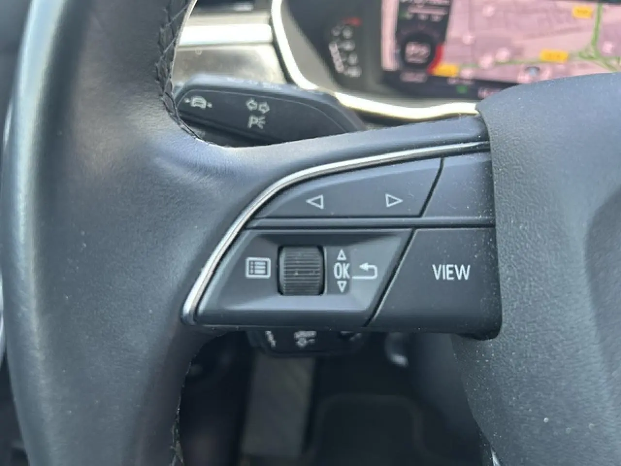 Gros plan sur les commandes gauche du volant cuir noir de l'Audi Q3 Sportback blanc, avec boutons de navigation et affichage.