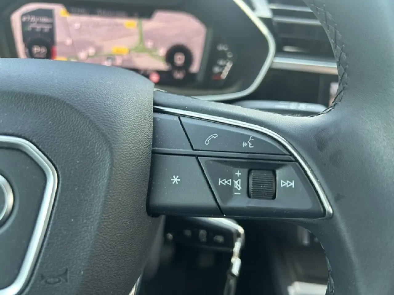 Gros plan sur les commandes gauche du volant cuir noir de l'Audi Q3 Sportback blanc avec affichage numérique en arrière-plan.