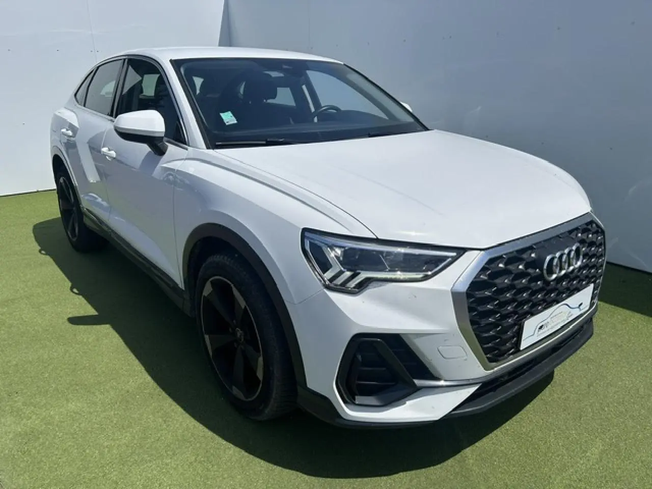 Audi Q3 Sportback blanc en 3/4 avant droit, avec calandre grenue noire et jantes aluminium noires 5 branches doubles.