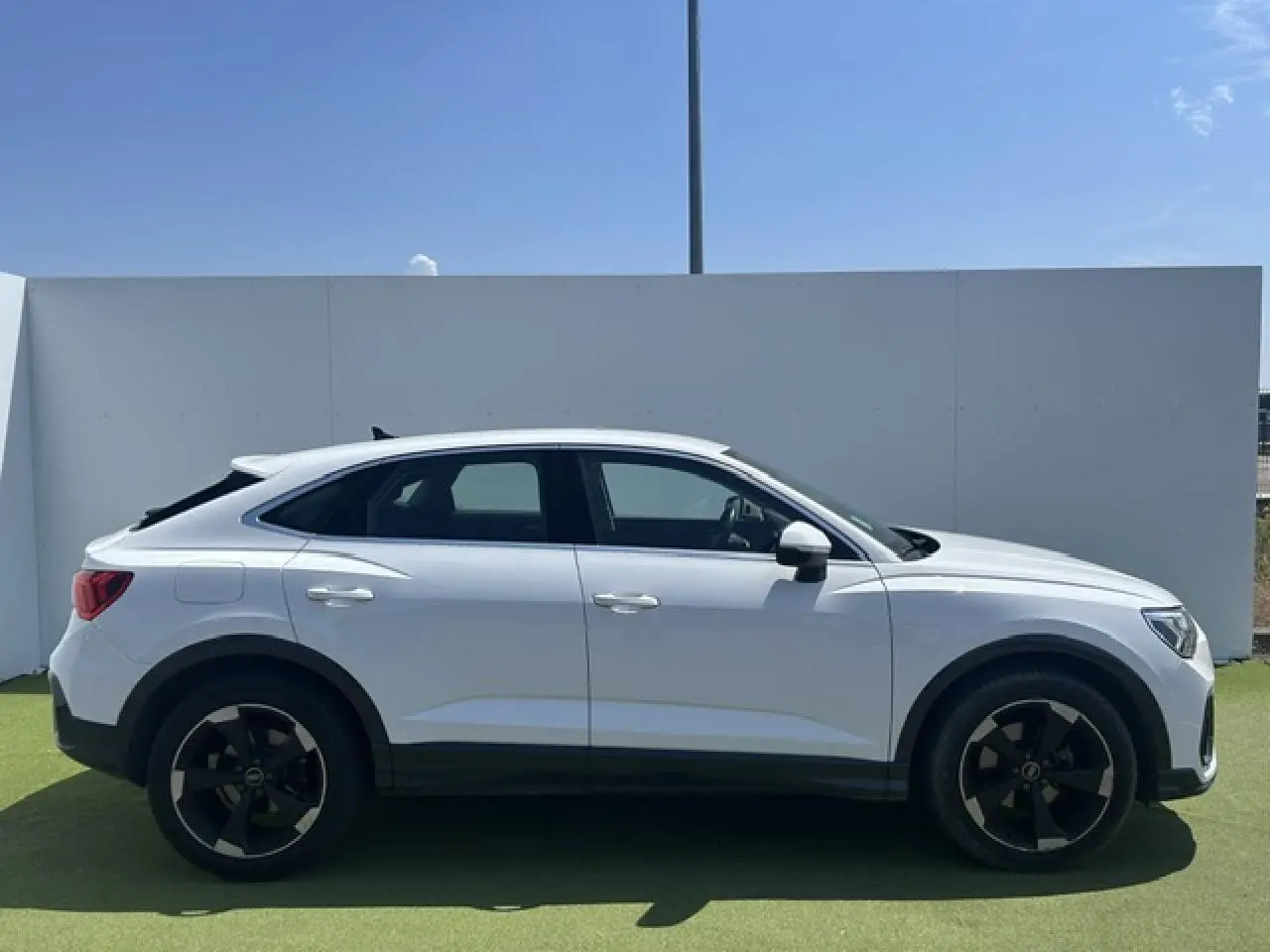 Audi Q3 Sportback blanc vue de profil côté gauche, avec jantes noires et toit plongeant distinctif.