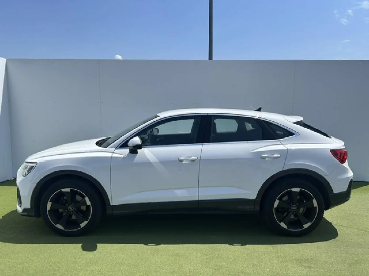 Profil droit d'un Audi Q3 Sportback blanc 2022 avec jantes noires et toit plongeant, sur fond extérieur clair.