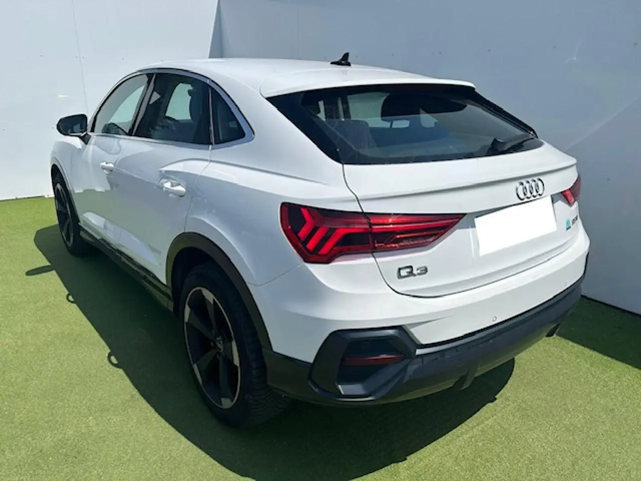 Audi Q3 Sportback blanc en 3/4 arrière droit, avec feux LED et jantes noires distinctives.