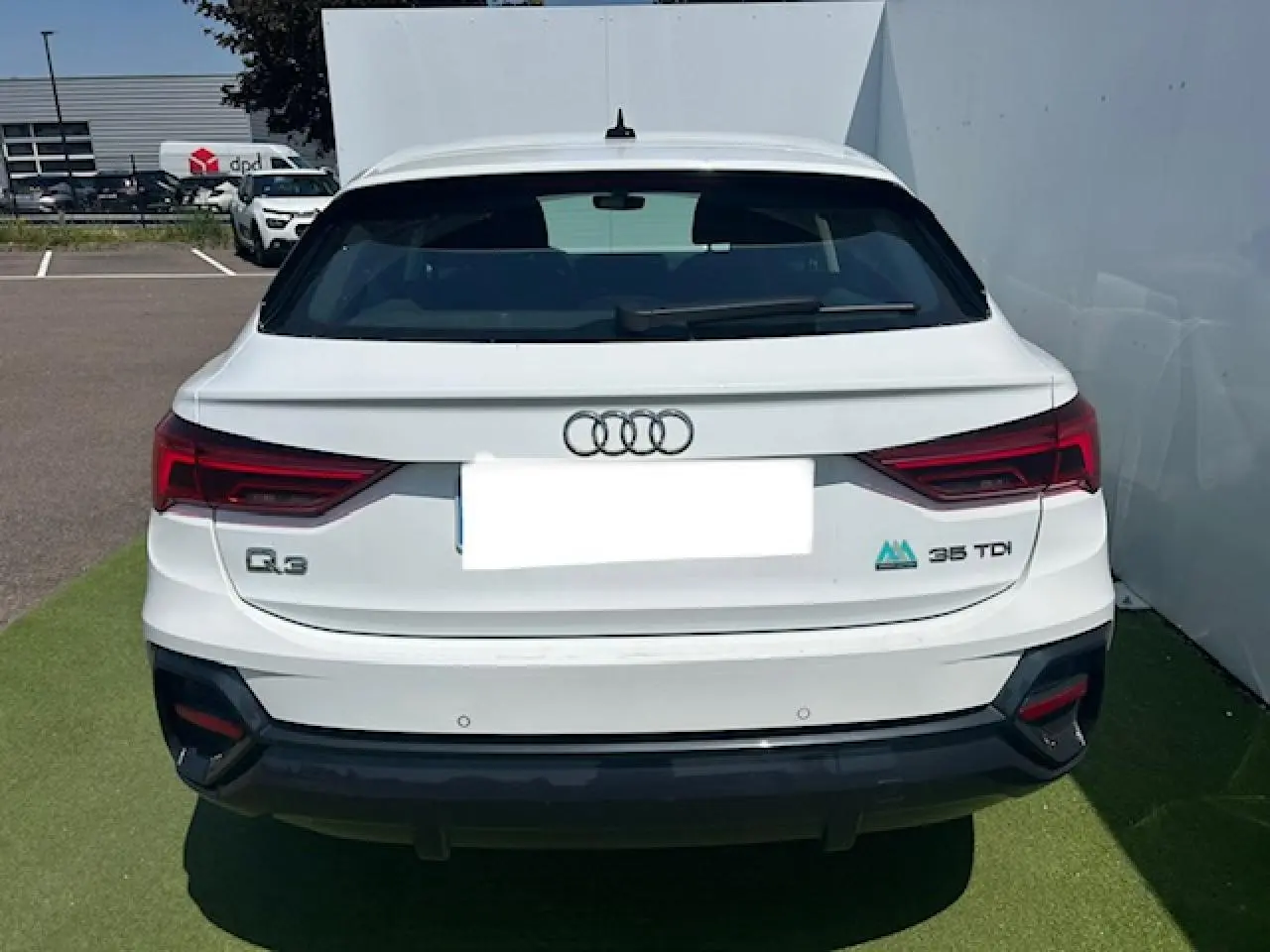 Vue arrière d'un Audi Q3 blanc 35 TDI avec feux LED et logo distinctif sur un parking extérieur.