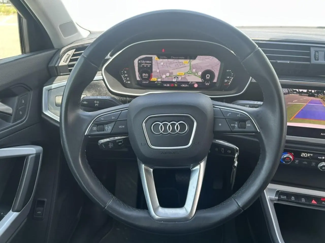 Vue intérieure centrée sur le volant noir multifonctions d’un Audi Q3 2022 avec tableau de bord numérique et écran de caméra de recul.