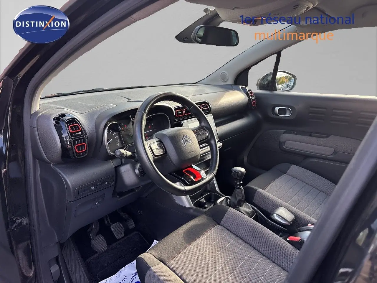 Vue intérieure côté conducteur du Citroën C3 Aircross noir, avec volant multifonction et détails rouges sur les aérateurs.