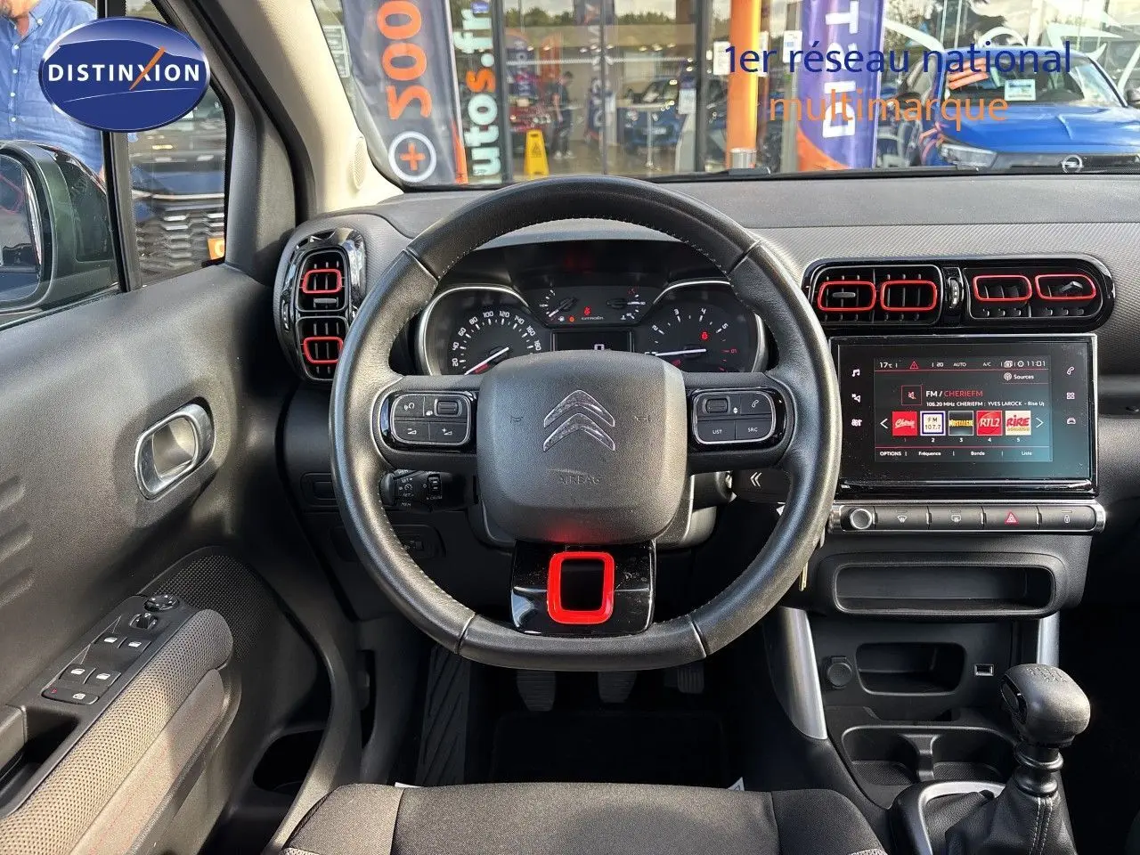 Intérieur de Citroën C3 Aircross 2019, vue frontale du volant noir avec touches rouges et écran tactile central allumé.