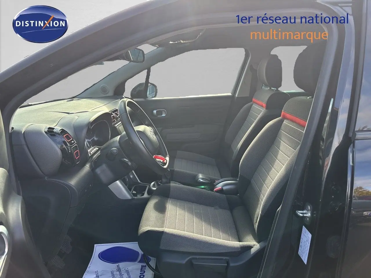 Vue intérieure côté conducteur d’un Citroën C3 Aircross noir Perla Metal 2019, sièges tissu noir avec bande rouge.