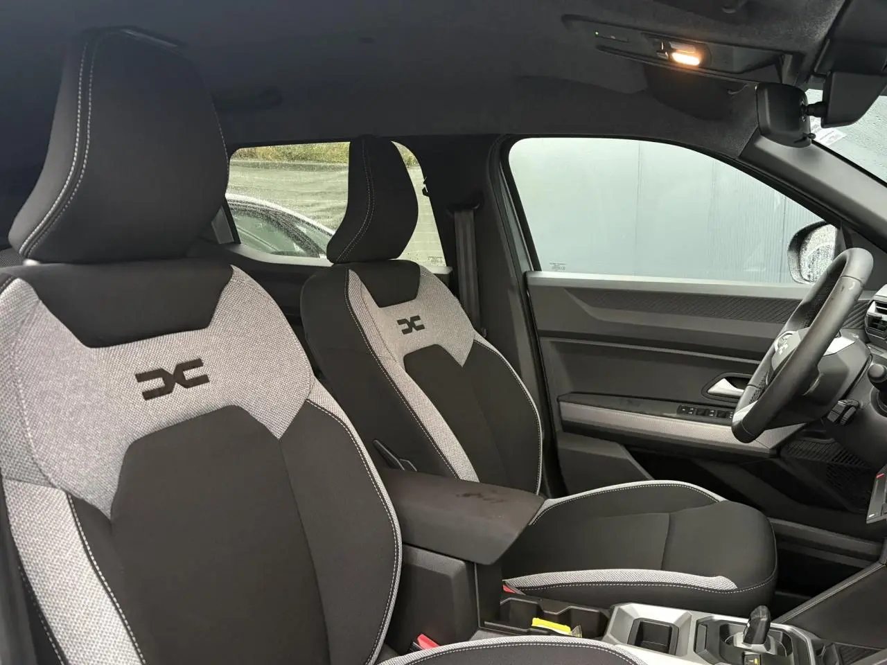 Vue intérieure côté droit du Dacia Duster 2026, sièges bi-matière gris clair et noir avec logo distinctif brodé.