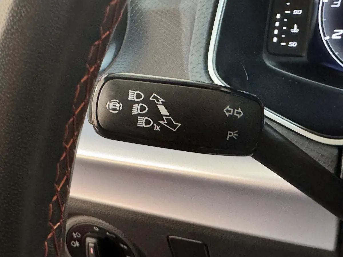 Gros plan sur la manette de commande des phares et clignotants, volant cuir rouge partiellement visible.