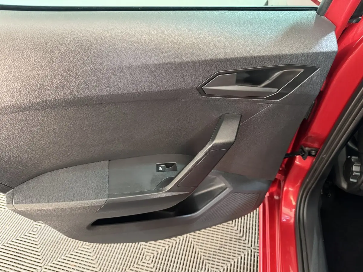 Vue intérieure côté gauche de la porte avant rouge d'une SEAT IBIZA 1.0 TSI 110 FR avec poignée noire et bouton de lève-vitre.