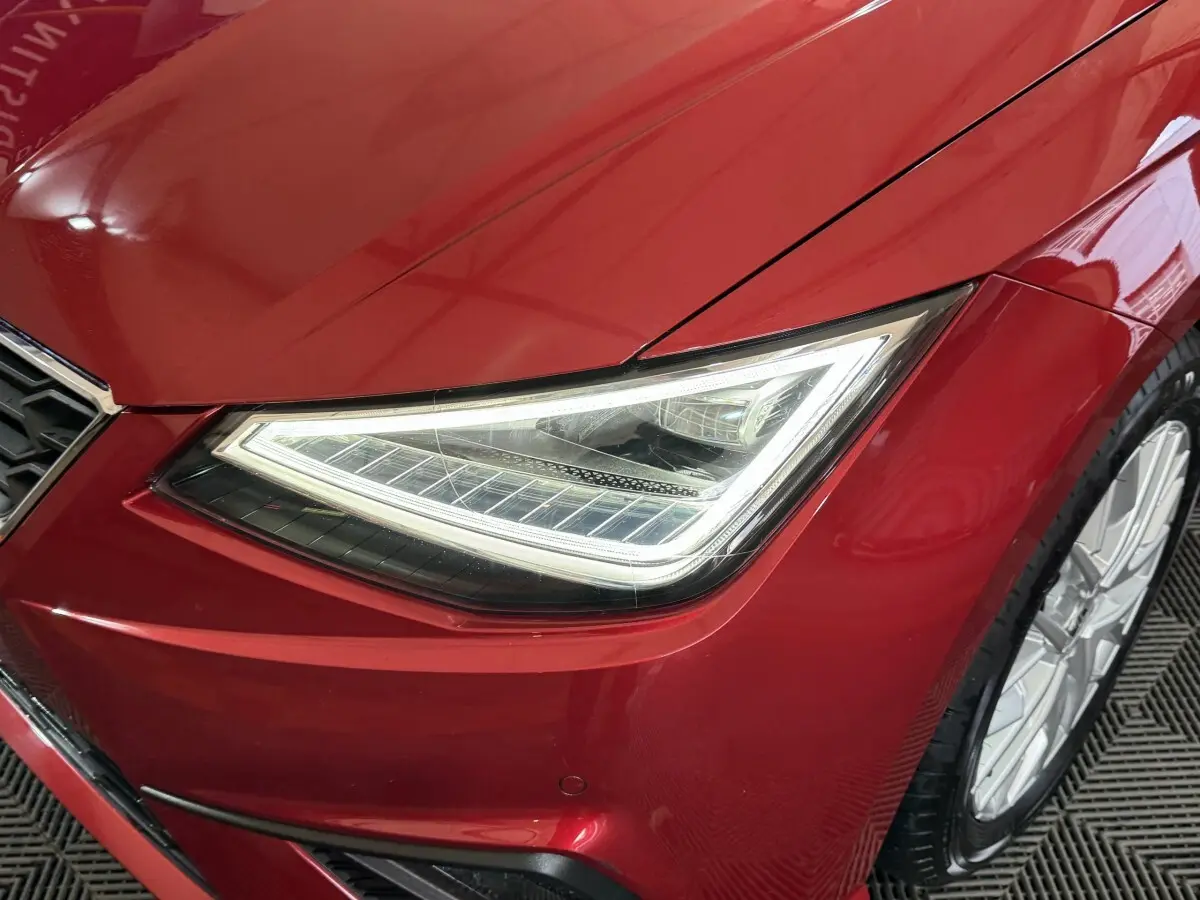 Gros plan sur le phare avant droit allumé d’une SEAT Ibiza 1.0 TSI 110 FR rouge 2024 avec jante alu visible.