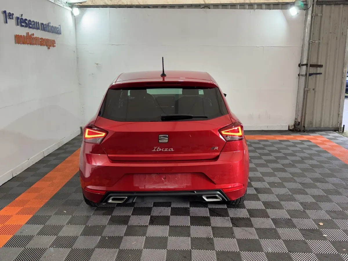 Vue arrière d'une SEAT Ibiza 1.0 TSI 110 FR rouge, feux LED allumés et double sortie d'échappement chromée.