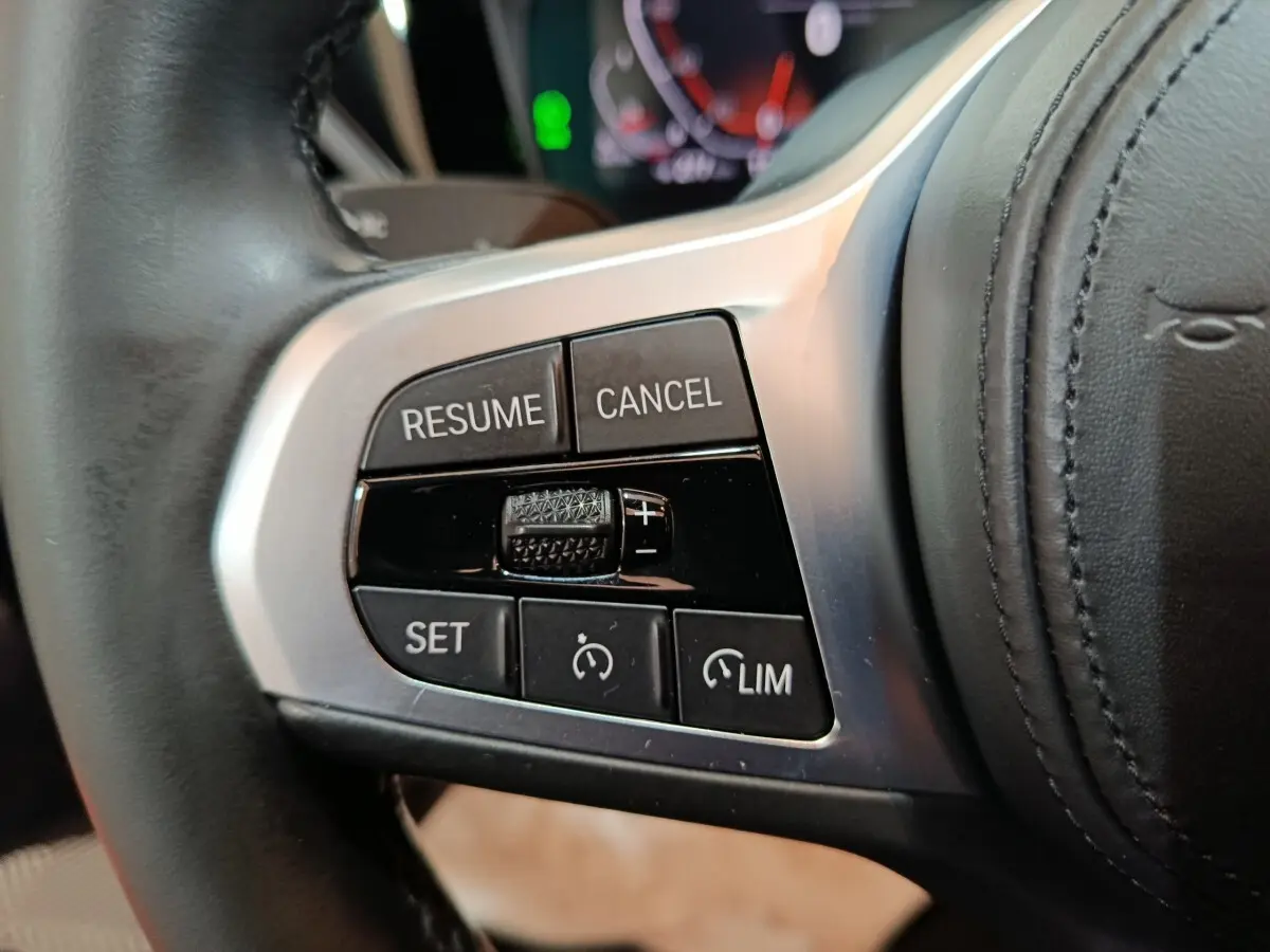 Gros plan sur les commandes de régulateur de vitesse à gauche du volant cuir d’une BMW Série 3 gris clair 2022.