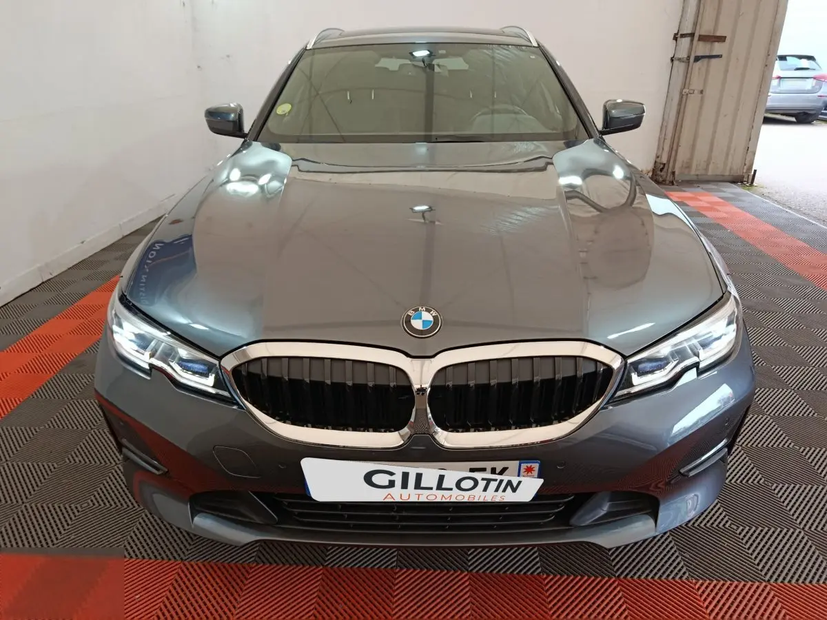 Vue avant d'une BMW Série 3 318d gris clair avec calandre double haricot et phares LED allumés.